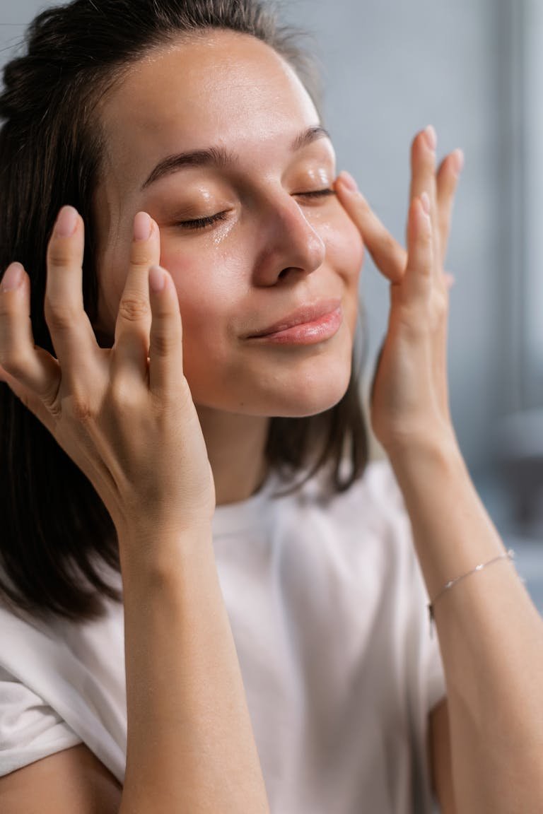 Young woman applying skincare cream with a smile, highlighting self-care and beauty routines.